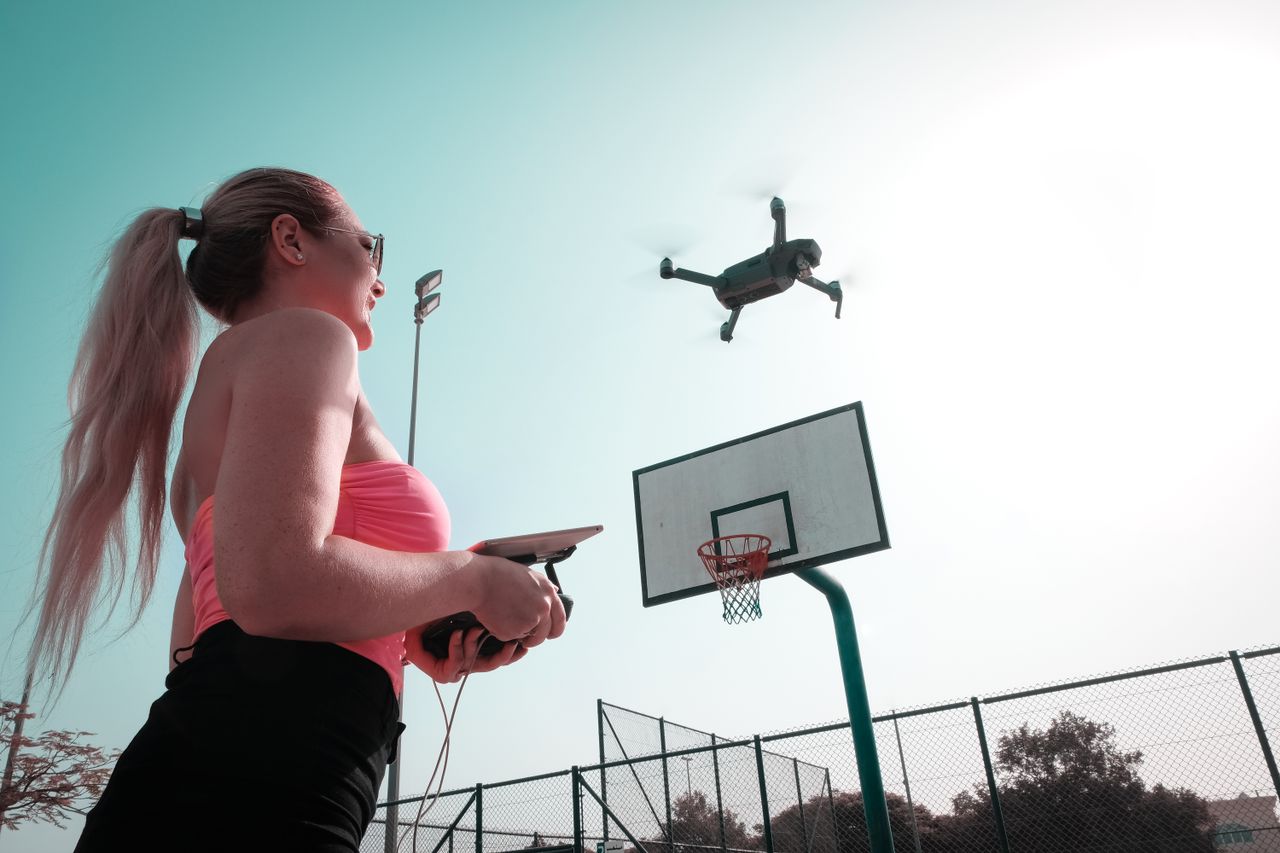 Services A woman pilots a drone at an outdoor basketball court, enjoying a sunny day with leisure activities.